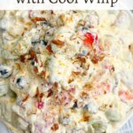 fruit salad recipe with cool whip topped with coconut and pecans in a white bowl