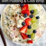 fruit salad recipe with cool whip topped with coconut and pecans and fruit in a white bowl
