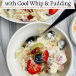 small white bowl of cool whip fruit salad with larger bowl of salad in background