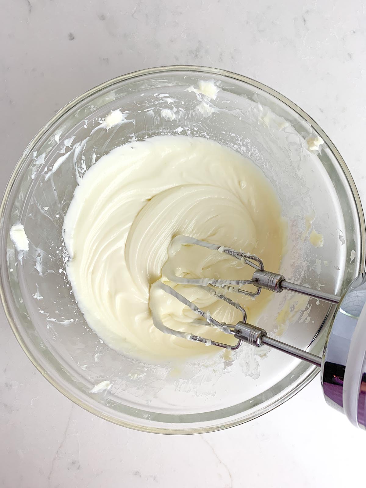 white chocolate cream cheese frosting in clear bowl with mixer
