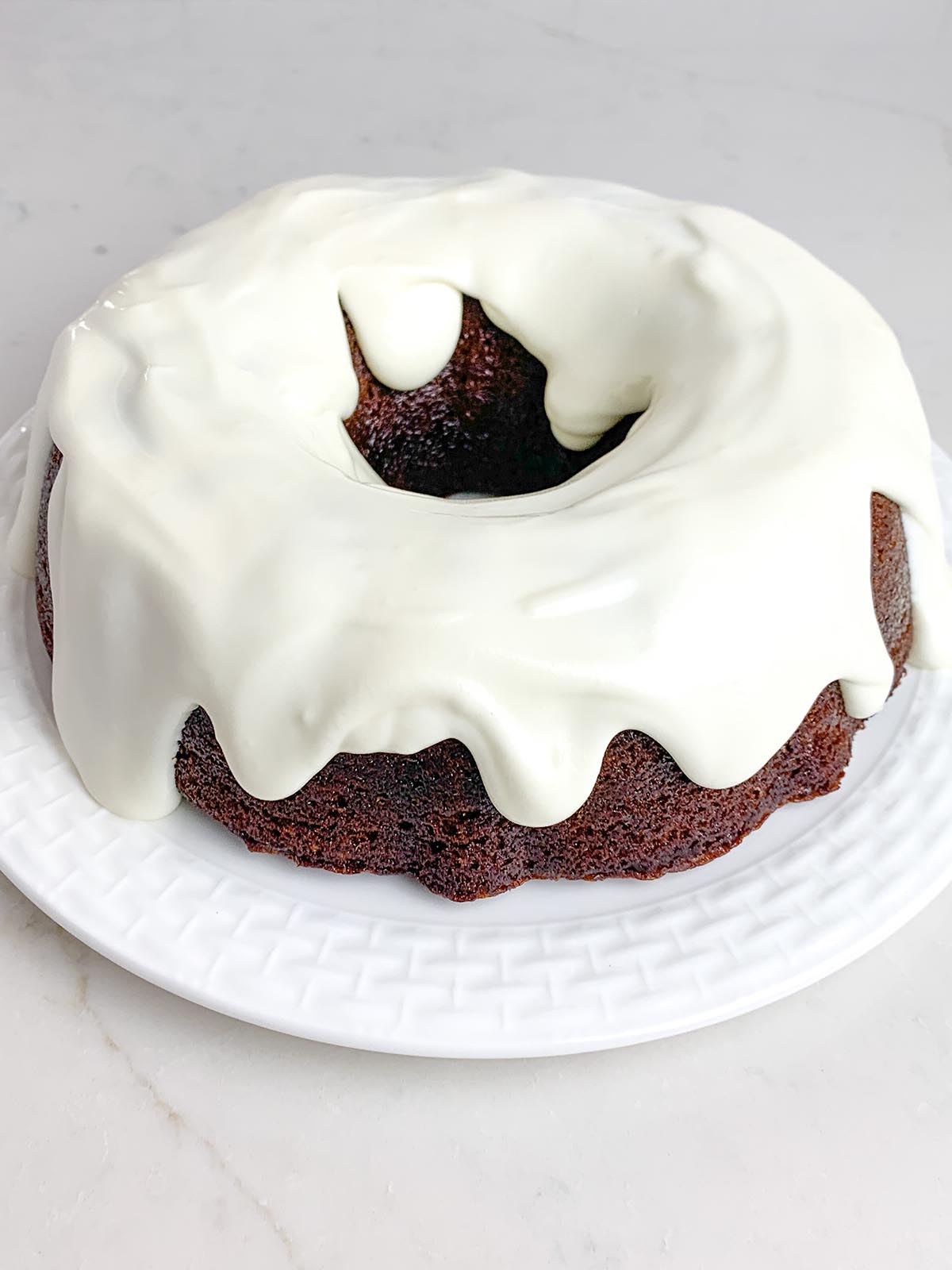 gingerbread bundt cake with white chocolate cream cheese frosting on a white plate