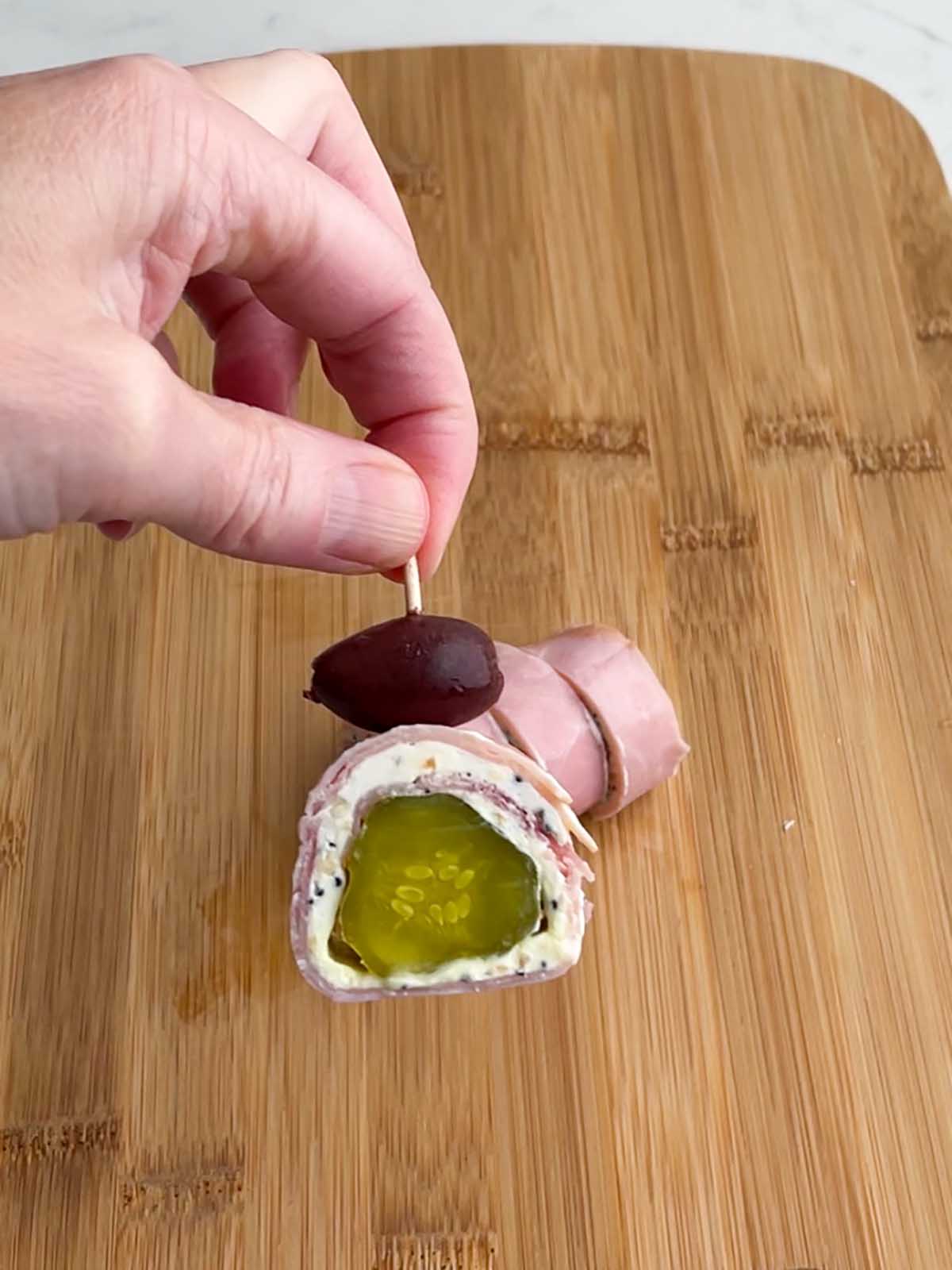hand holding a ham pickle roll with an olive on top