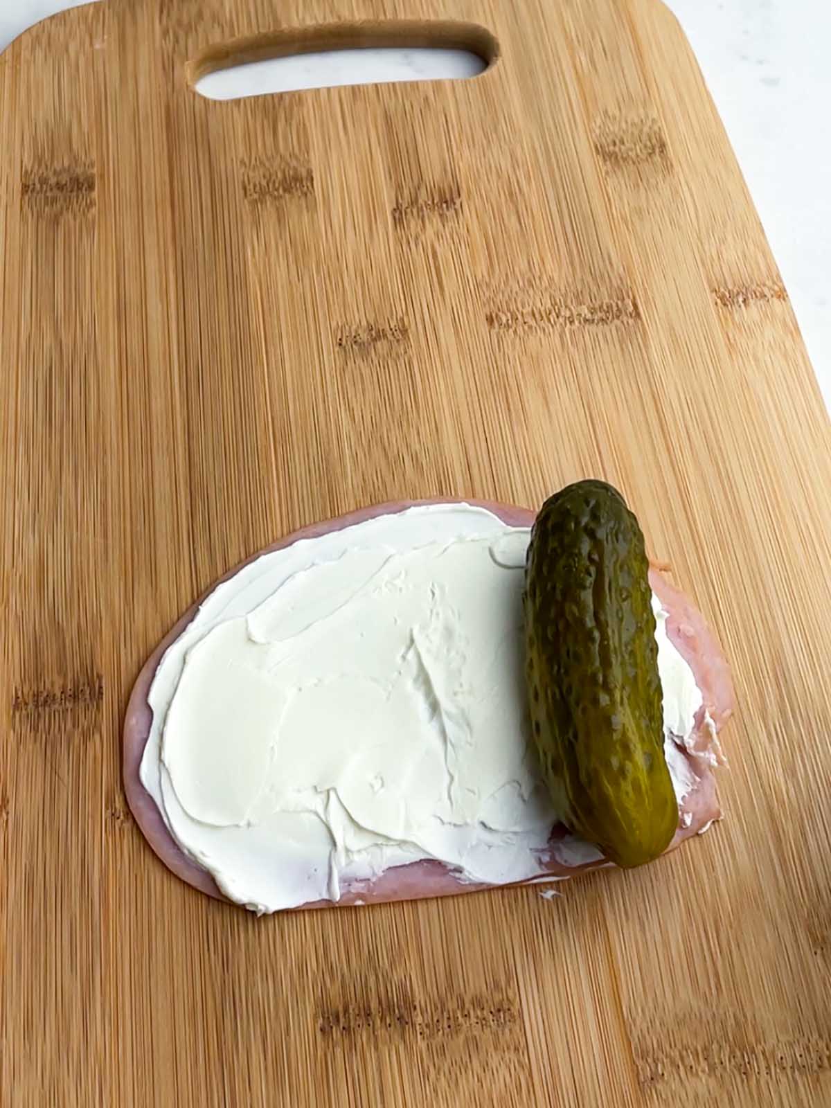 cream cheese spread on a slice of ham with a pickle
