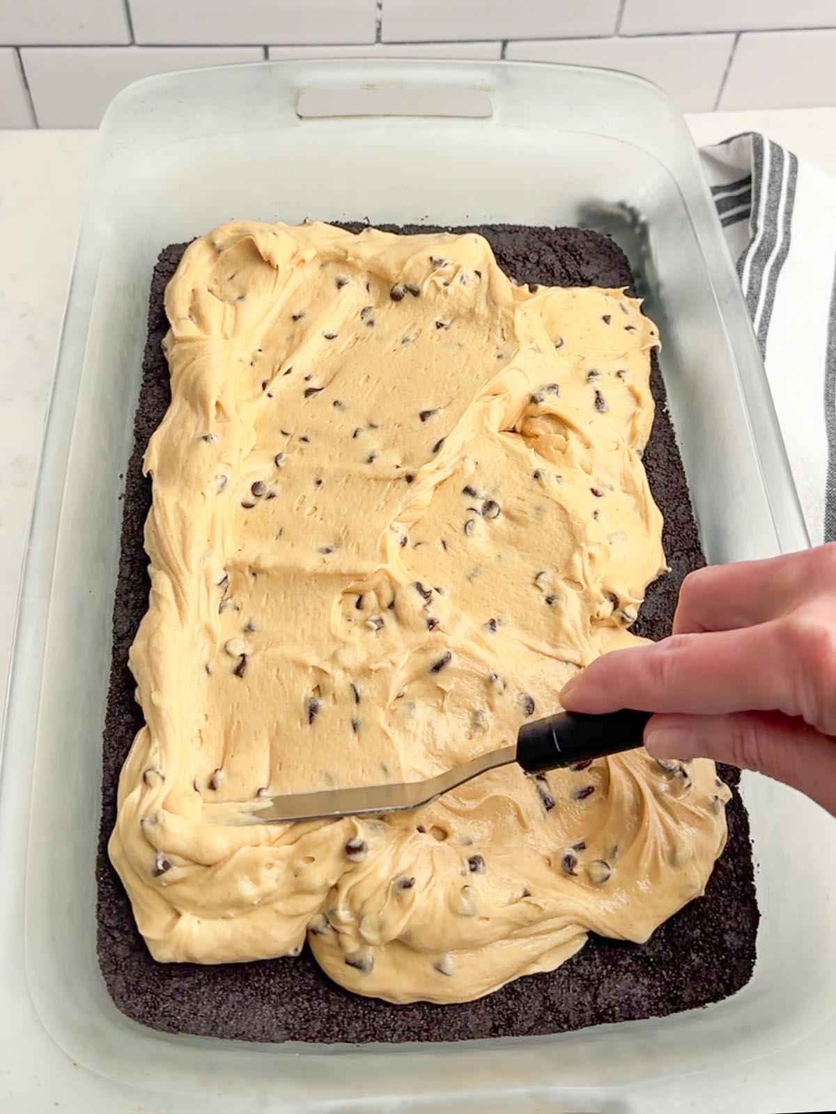 hand holding a spatula spreading peanut butter layer over Oreo layer