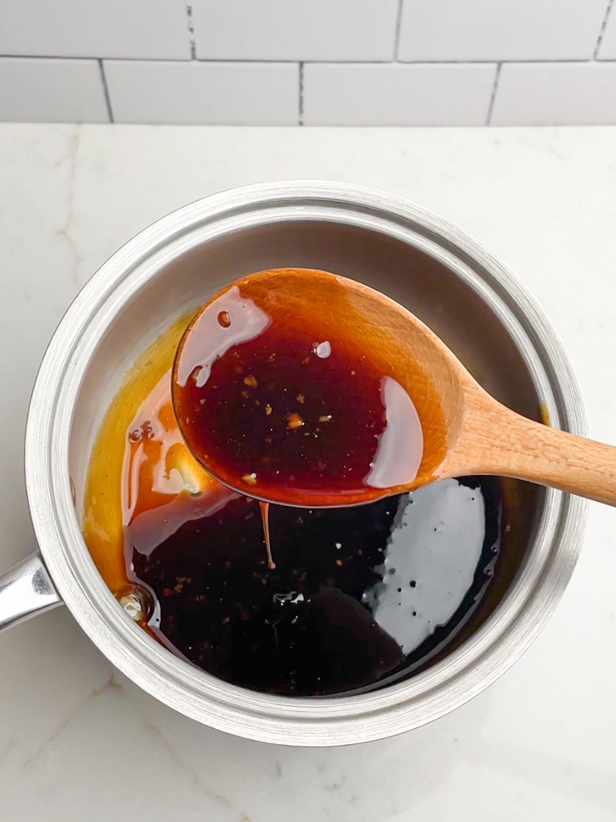 honey teriyaki sauce in a saucepan with wooden spoon full of sauce in foreground