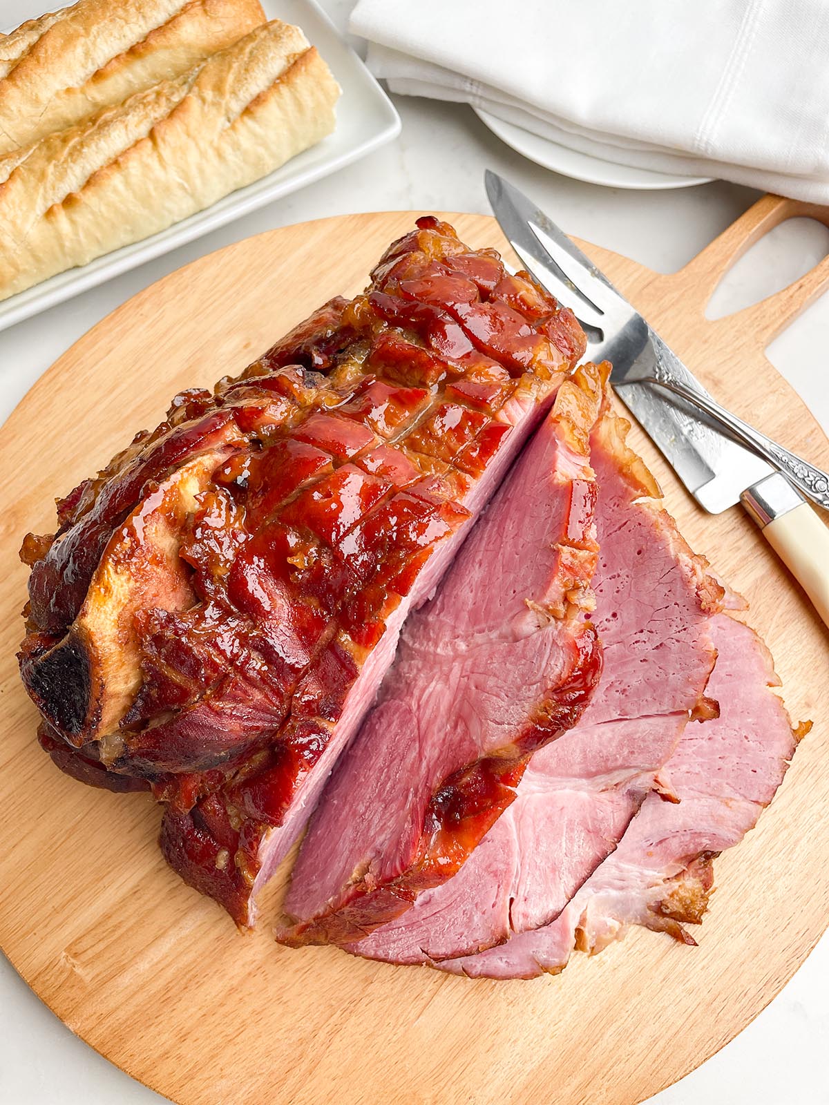 glazed roaster oven ham cut into slices on a wooden cutting board.