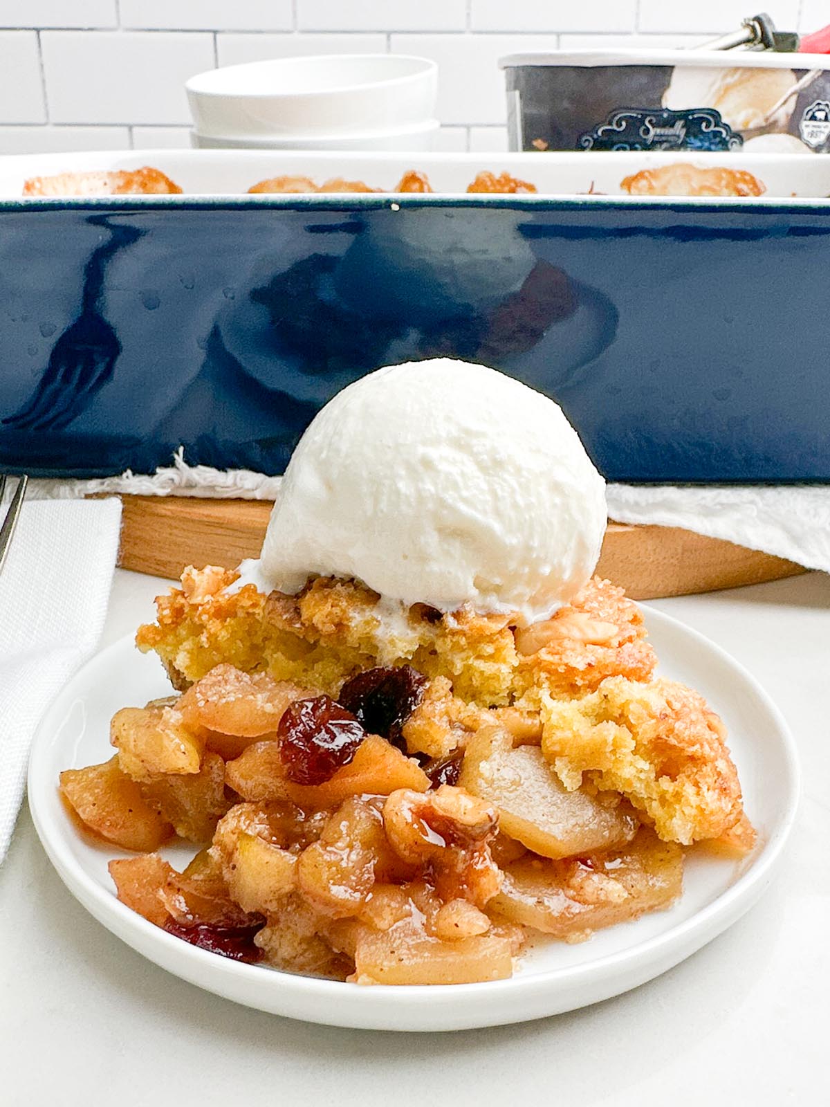 cake mix apple cobbler on a white plate with a scoop of vanilla ice cream on top.