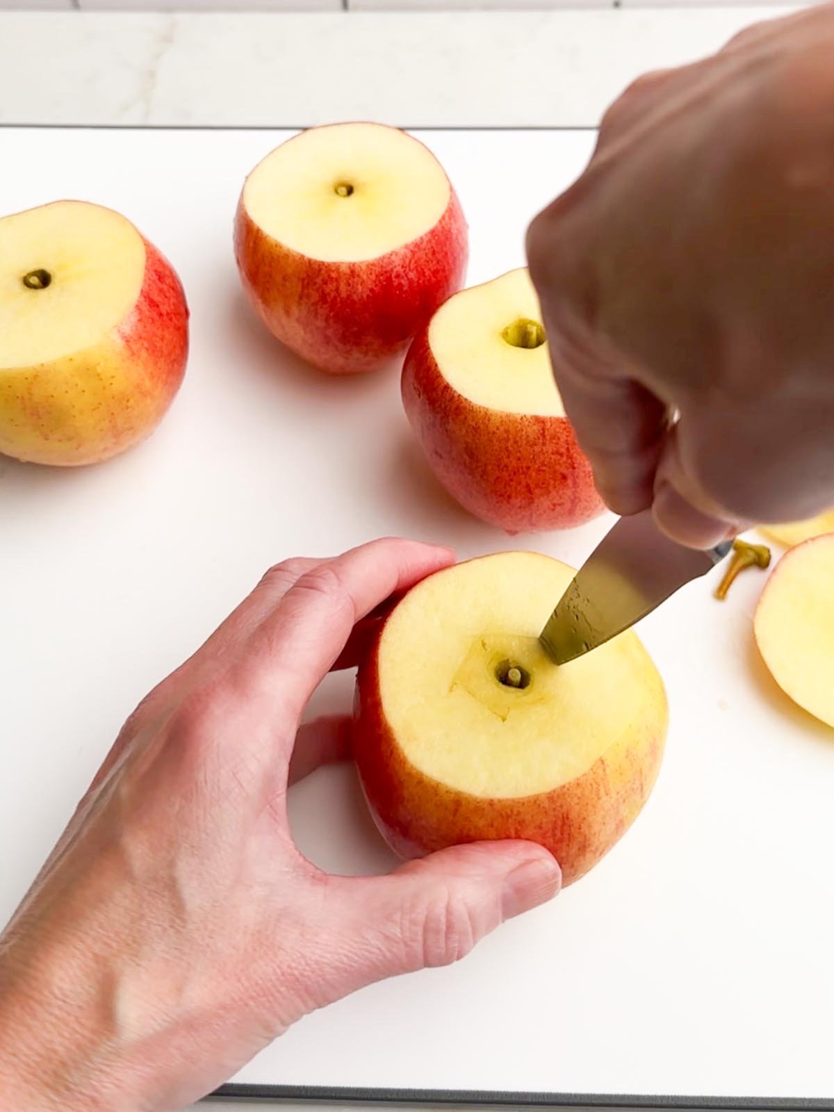 hands holding an apple and paring knife cutting out the core of an apple