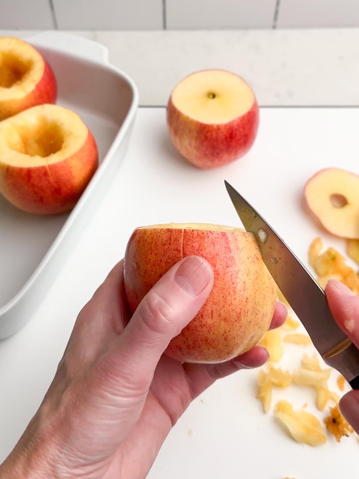 hands holding an apple and a paring knife scoring the skin of the apple