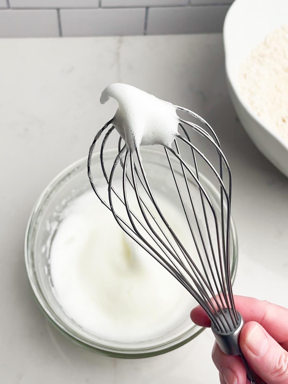 hand holding up a whisk with beaten egg whites.