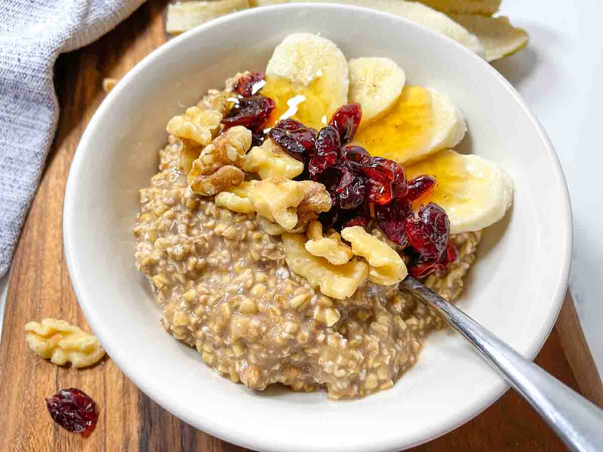 Cinnamon Banana Overnight Oats with walnuts, cranberries, bananas, and honey in a white bowl