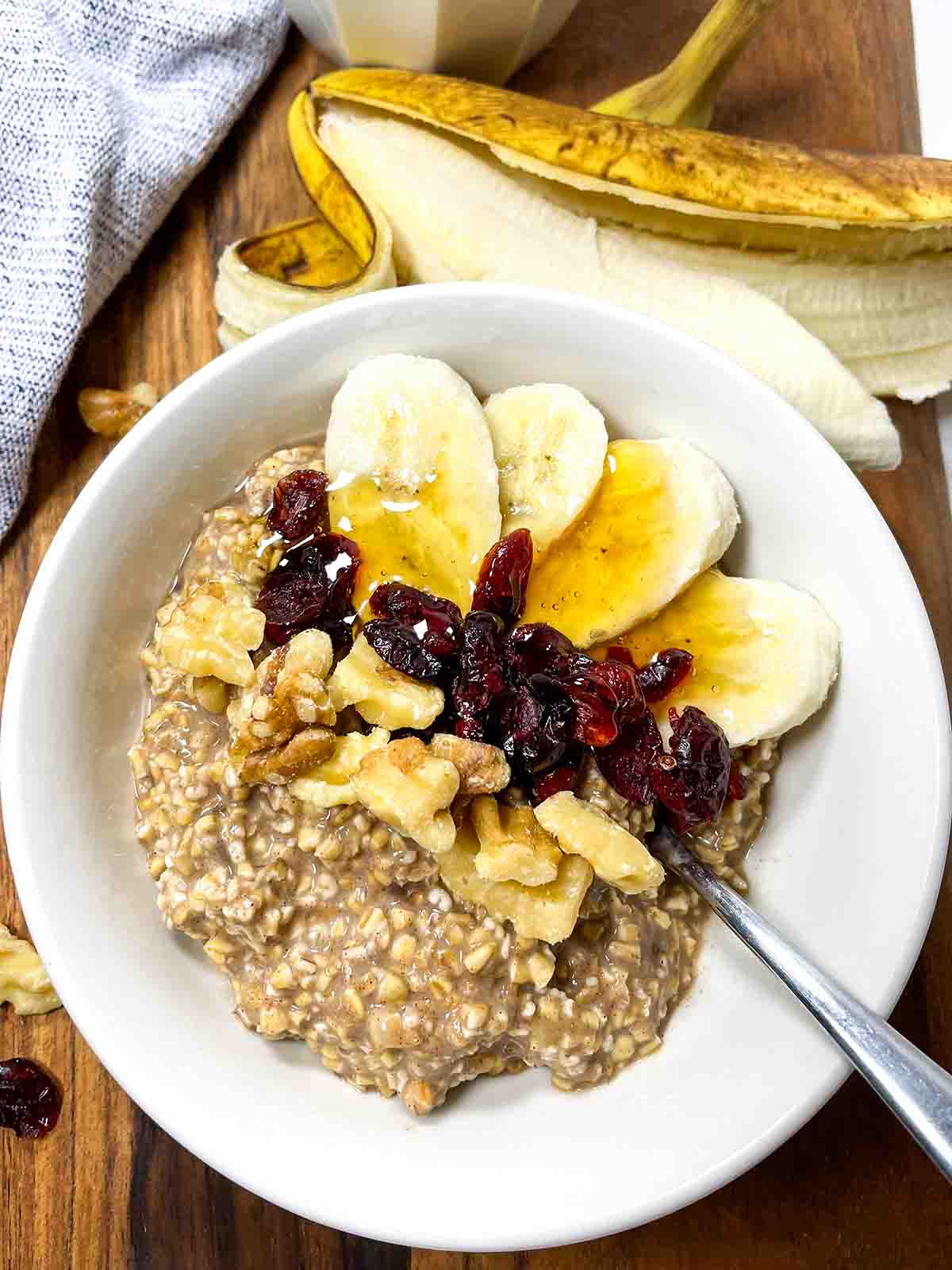 Cinnamon Banana Overnight Oats with banana, cranberries, walnuts, and honey in a white bowl 