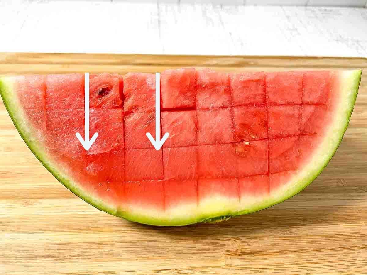 Watermelon quarter on a wooden cutting board with 2 white arrows pointing down