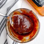jack daniels bbq sauce in a mason jar with a spoonful of sauce in foreground and bottle of jack daniels in background