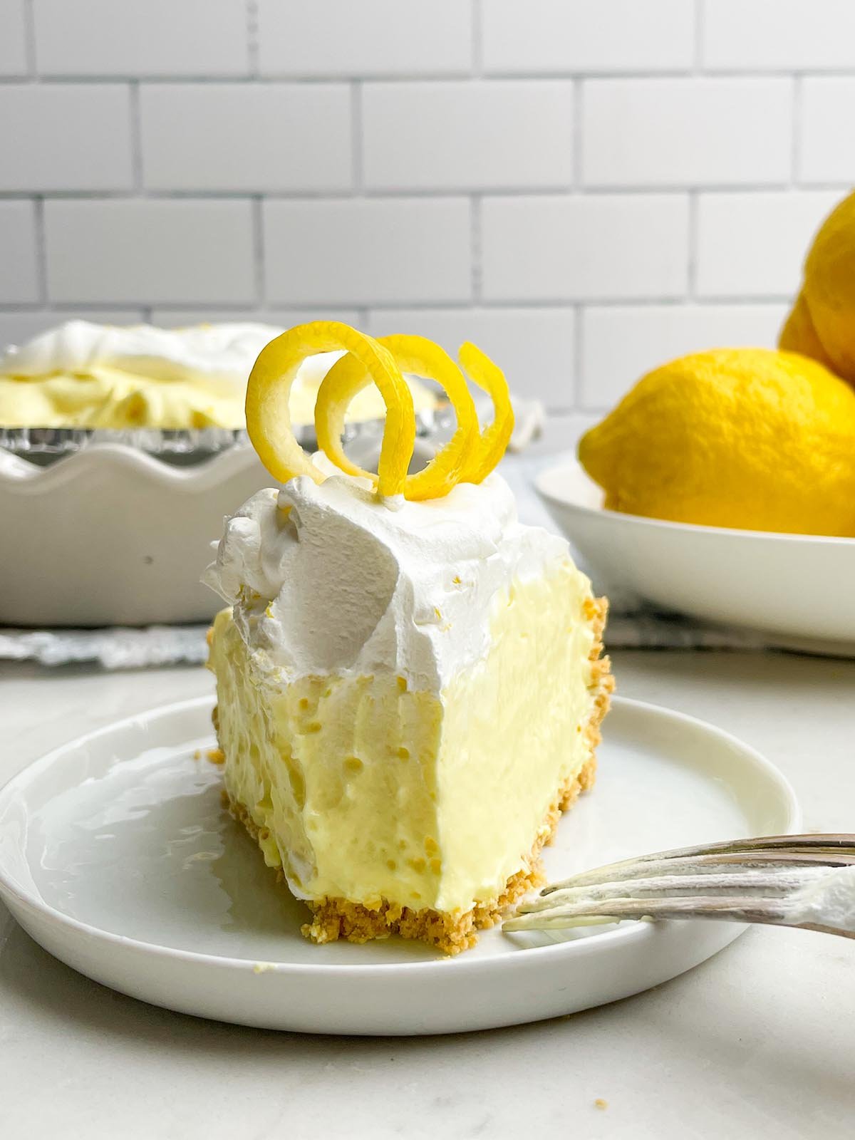 piece of Lemon jello pie on a white plate with a fork resting on it.