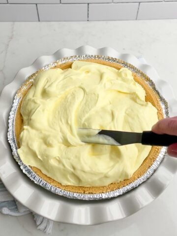 hand holding a spatula spreading jello pie filing into a graham cracker crust.