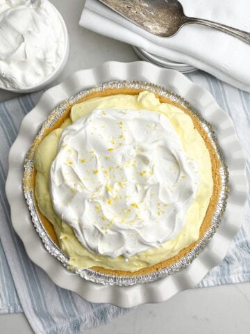 lemon jello pie topped with cool whip and lemon zest on a blue and white tea towel.