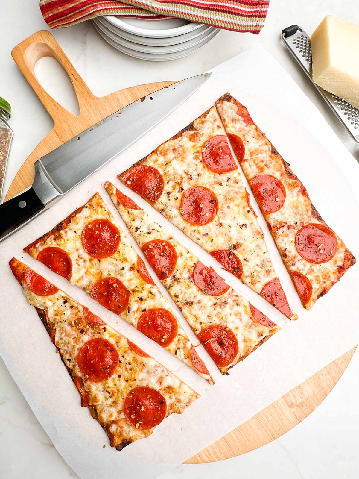 pepperoni lavash pizza cut into triangles on parchment on a wooden cutting board.