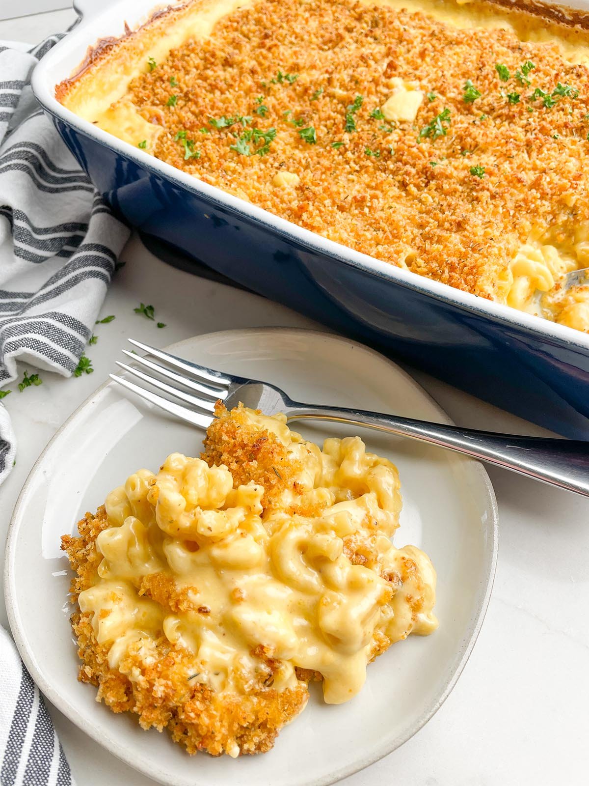 plate of macaroni and cheese next to casserole dish of macaroni and cheese with bread crumb topping.
