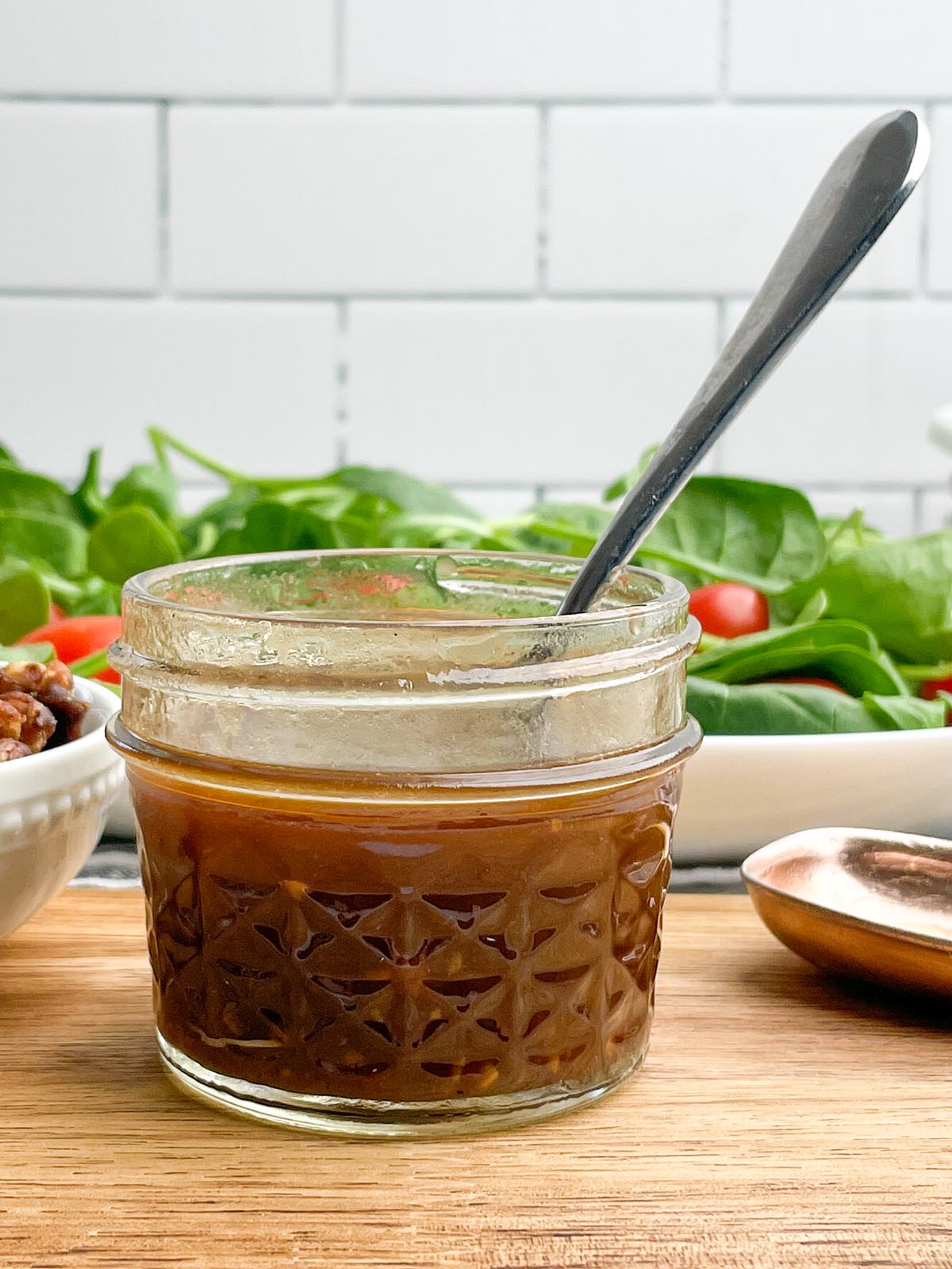 maple balsamic dressing in a short mason jar with a salad in the background