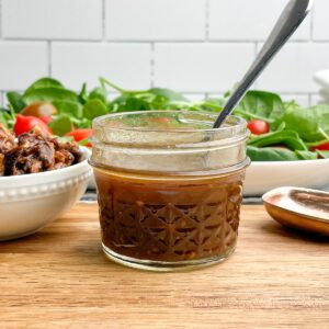 maple balsamic dressing in a short mason jar with a salad in the background