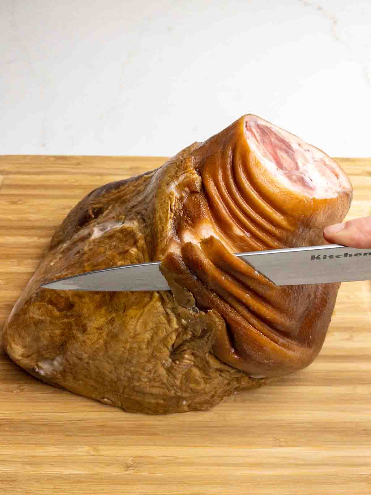 ham on a wooden cutting board with a knife cutting through the rind