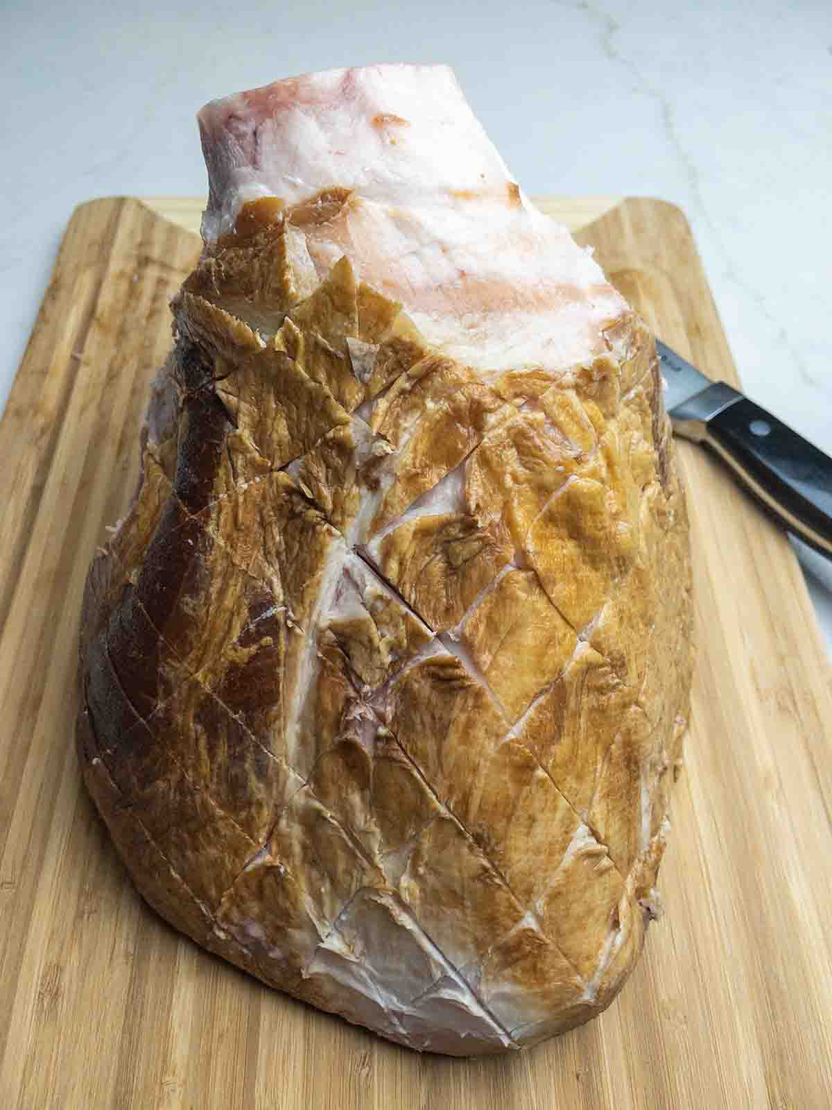 ham on a wooden cutting board with the fat layer scored into diamonds