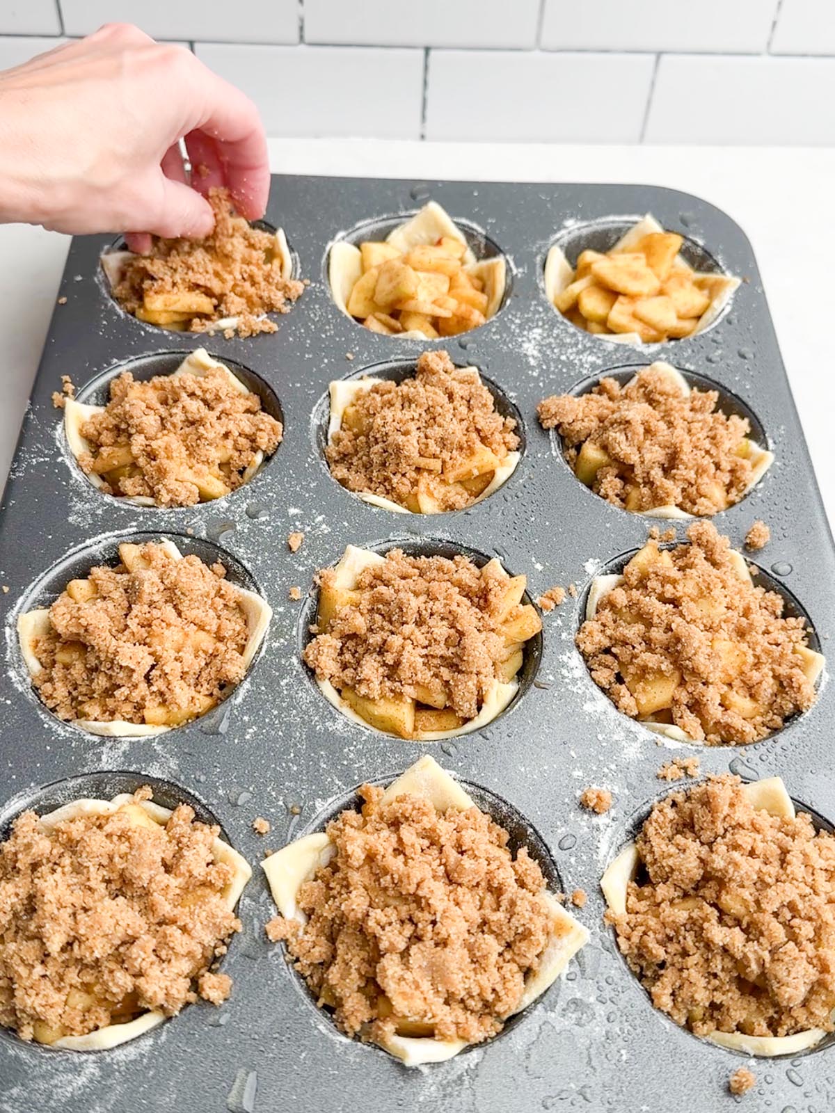 hand sprinkling crumble mixture on top of a puff pastry mini apple pie