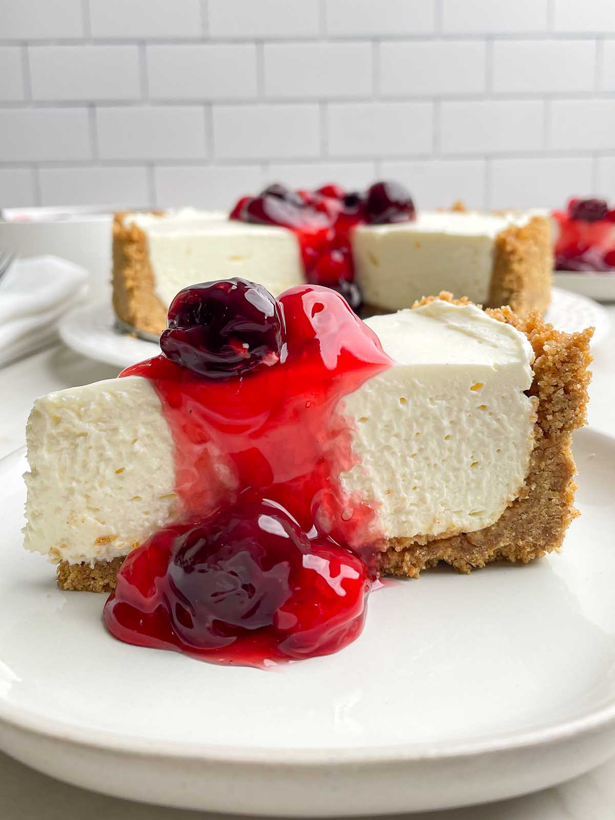 a piece of no bake cheesecake on a white plate with cherry topping.