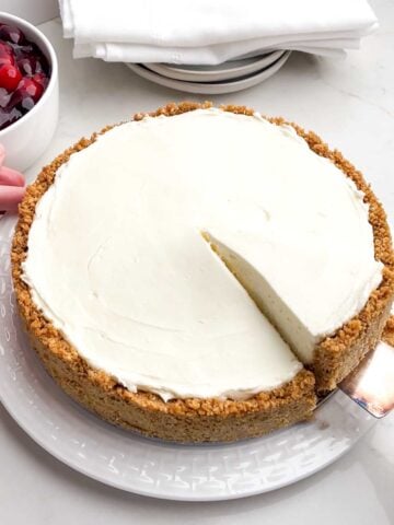A piece of No-Bake Cheesecake with Cool Whip being lifted out of the pan.