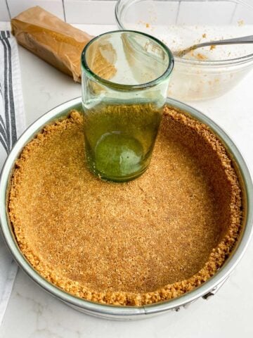 graham cracker crumbs pressed into a springform pan with a green glass.