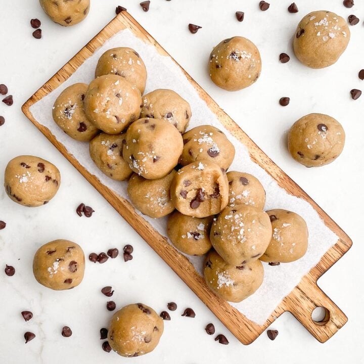 no bake chocolate chip cookie dough balls on a wooden cutting board surrounded by more cookie balls and chocolate chips