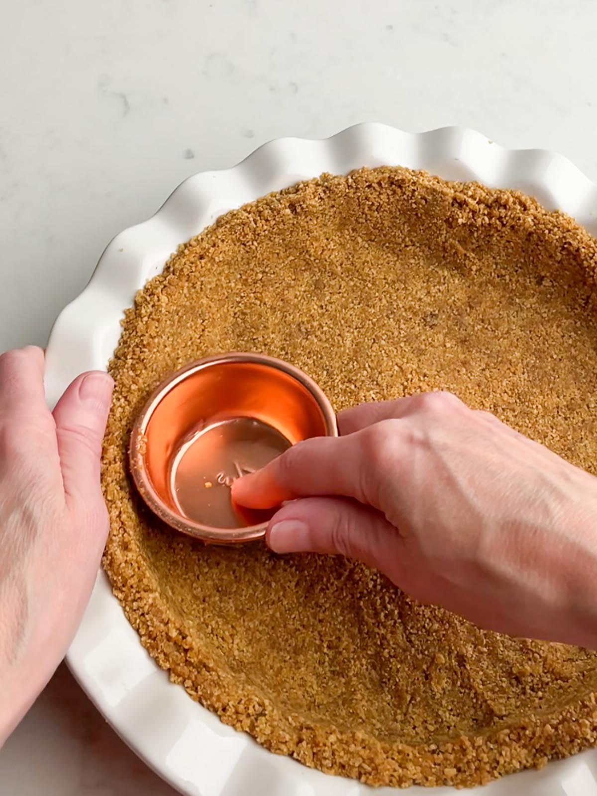 pressing graham cracker crust into pan with meausring cup