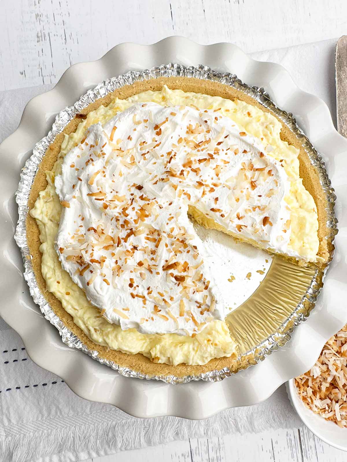 pineapple cream cheese pie topped with toasted coconut in a white pie plate