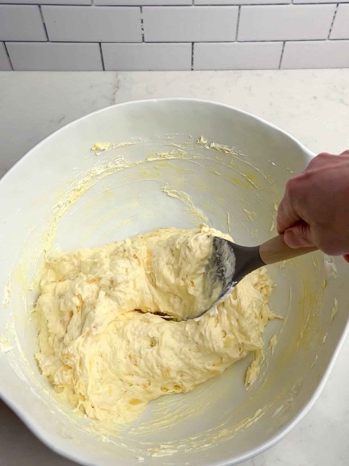 hand holding a spatula folding Cool Whip into the pineapple mixture in a white bowl
