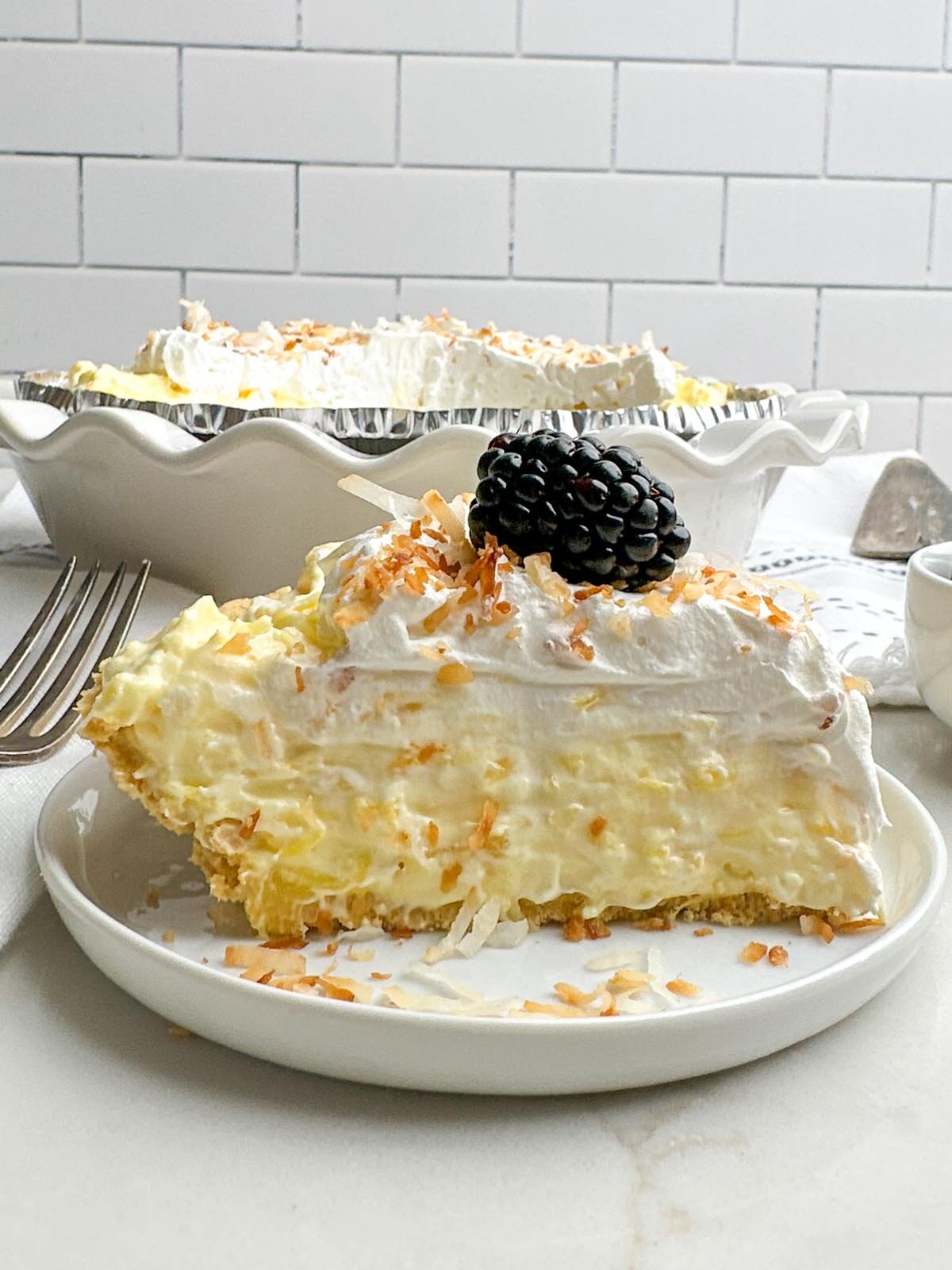 side view of white plate with piece of pineapple cream cheese pie topped with toasted coconut and a blackberry