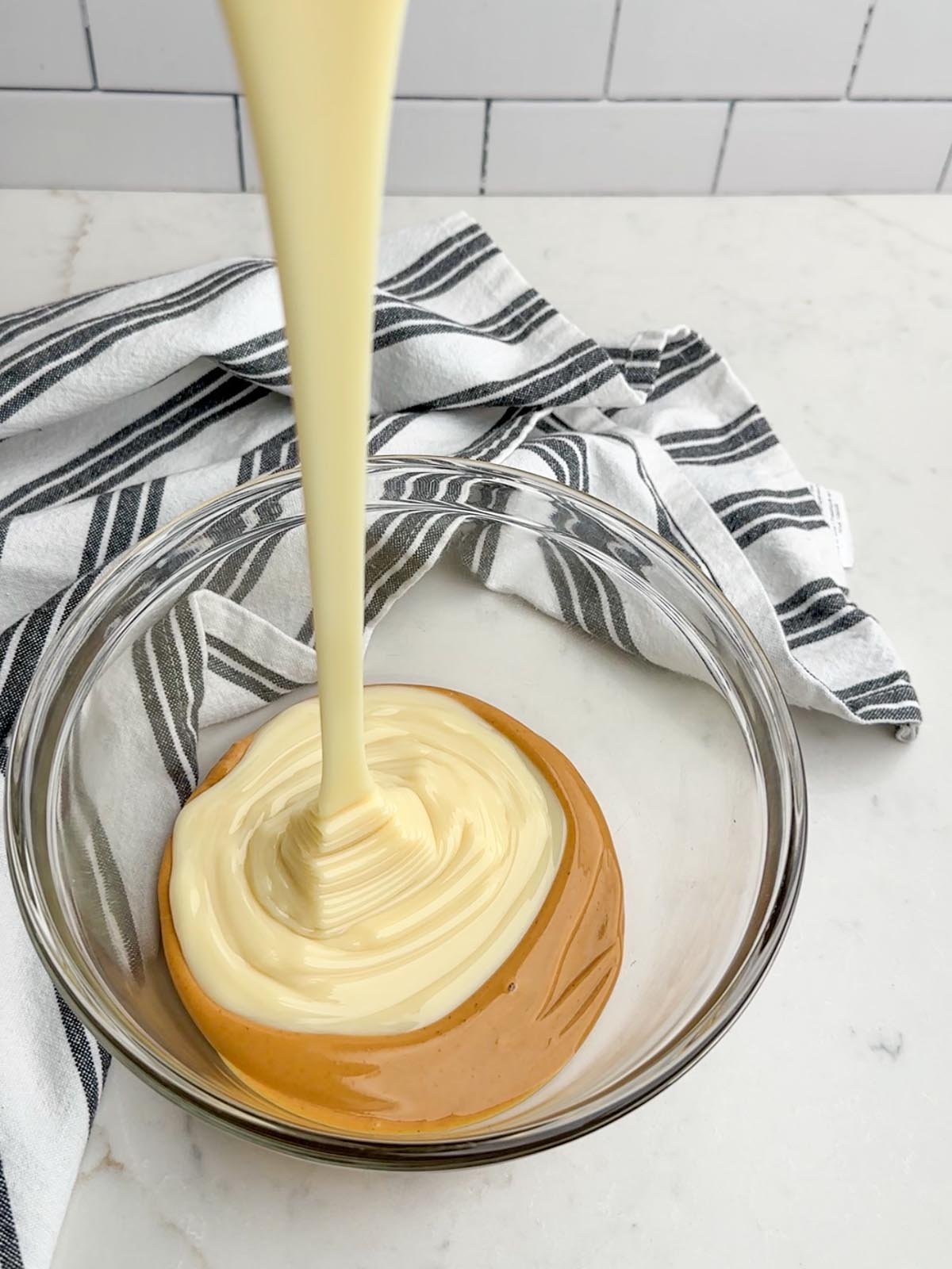 Condensed milk pouring into a bowl with melted peanut butter.