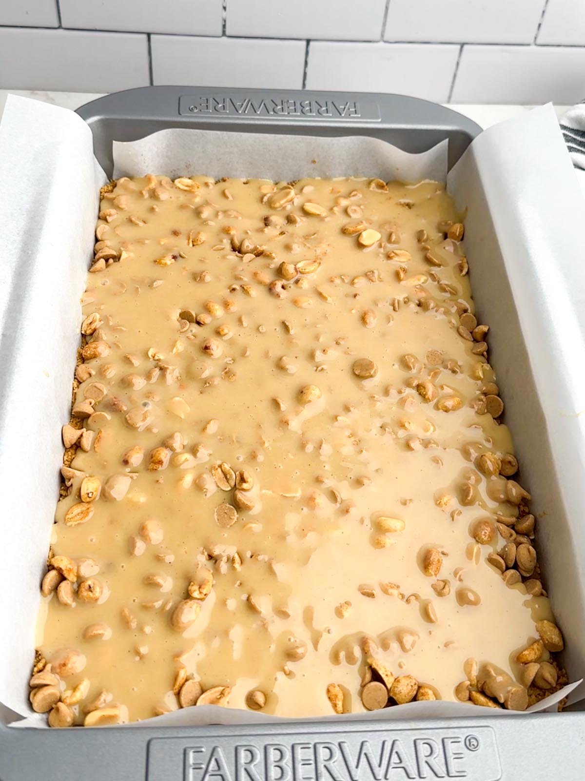 Peanut butter condensed milk layered over peanuts and peanut butter chips in a baking pan.