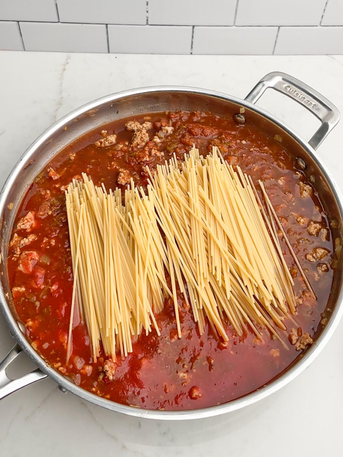 uncooked spaghetti noodles in skillet of taco meat and sauce
