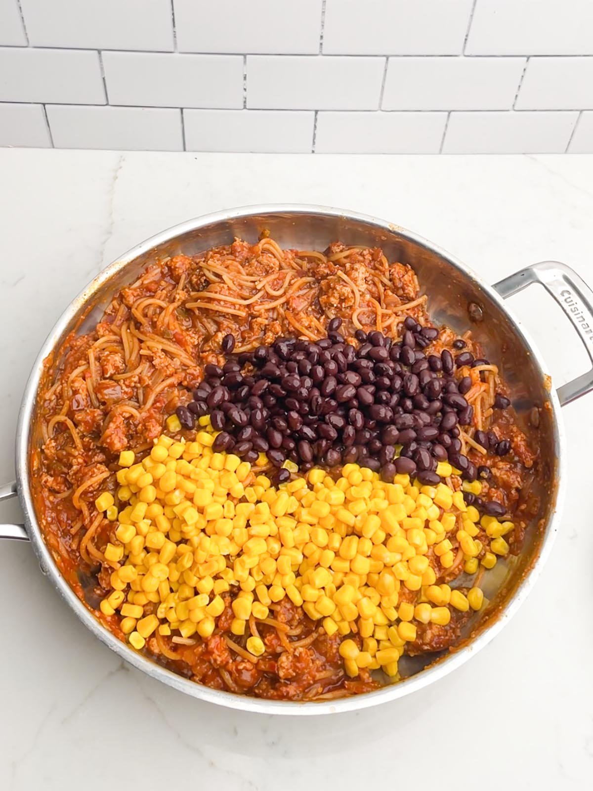 black beans and corn over taco spaghetti mixture in stainless steel skillet