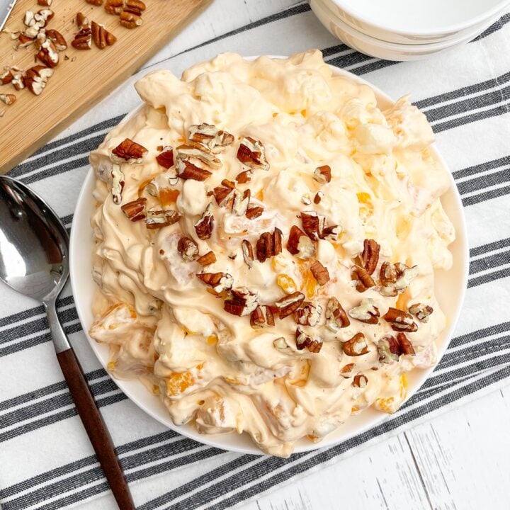 orange fluff salad topped with pecans in a white bowl