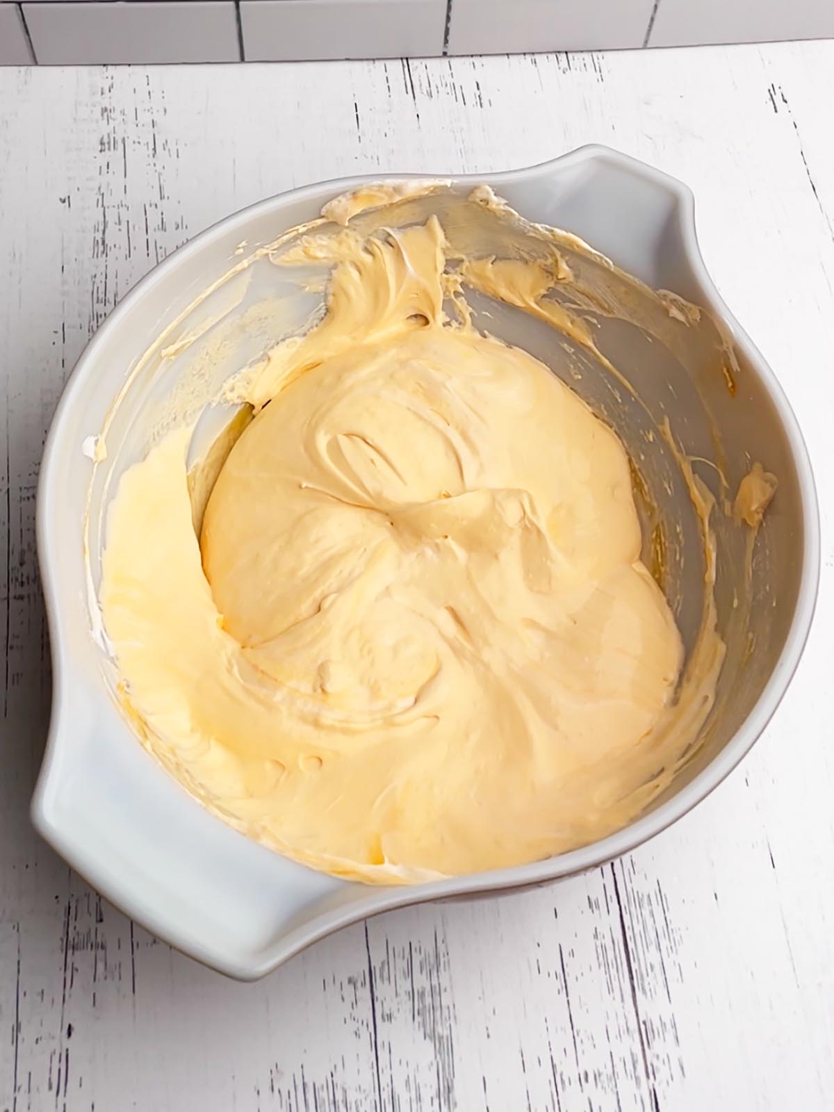orange pudding and cool whip mixture in a white mixing bowl