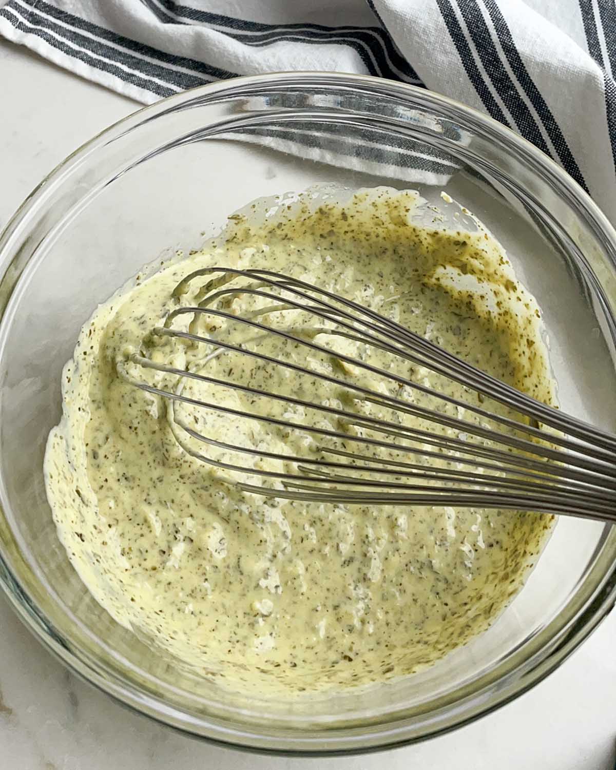 clear bowl with pesto mayo dressing ingredients and a whisk
