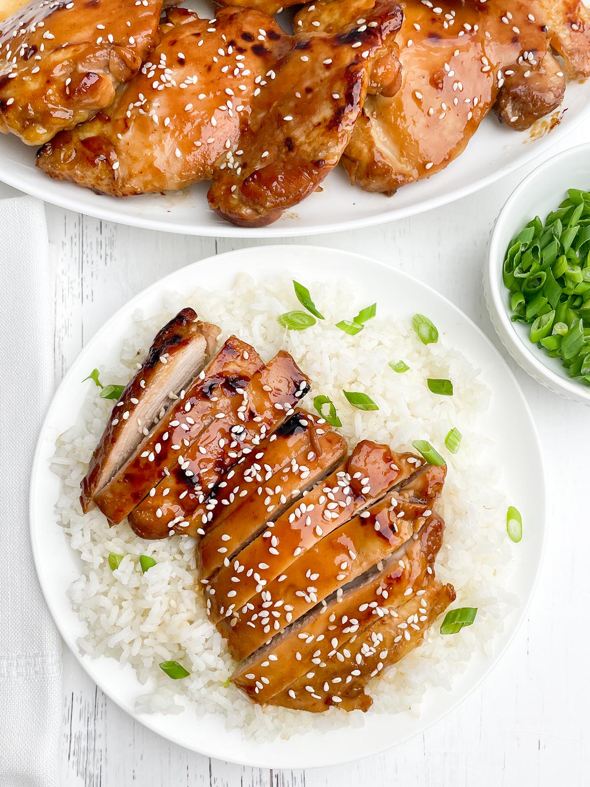 sliced oven baked teriyaki chicken with green onions and sesame seeds on a bed of rice.