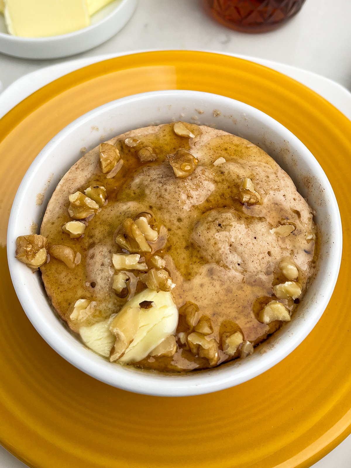 banana cinnamon walnut pancake in a mug with nuts, butter, and syrup on top
