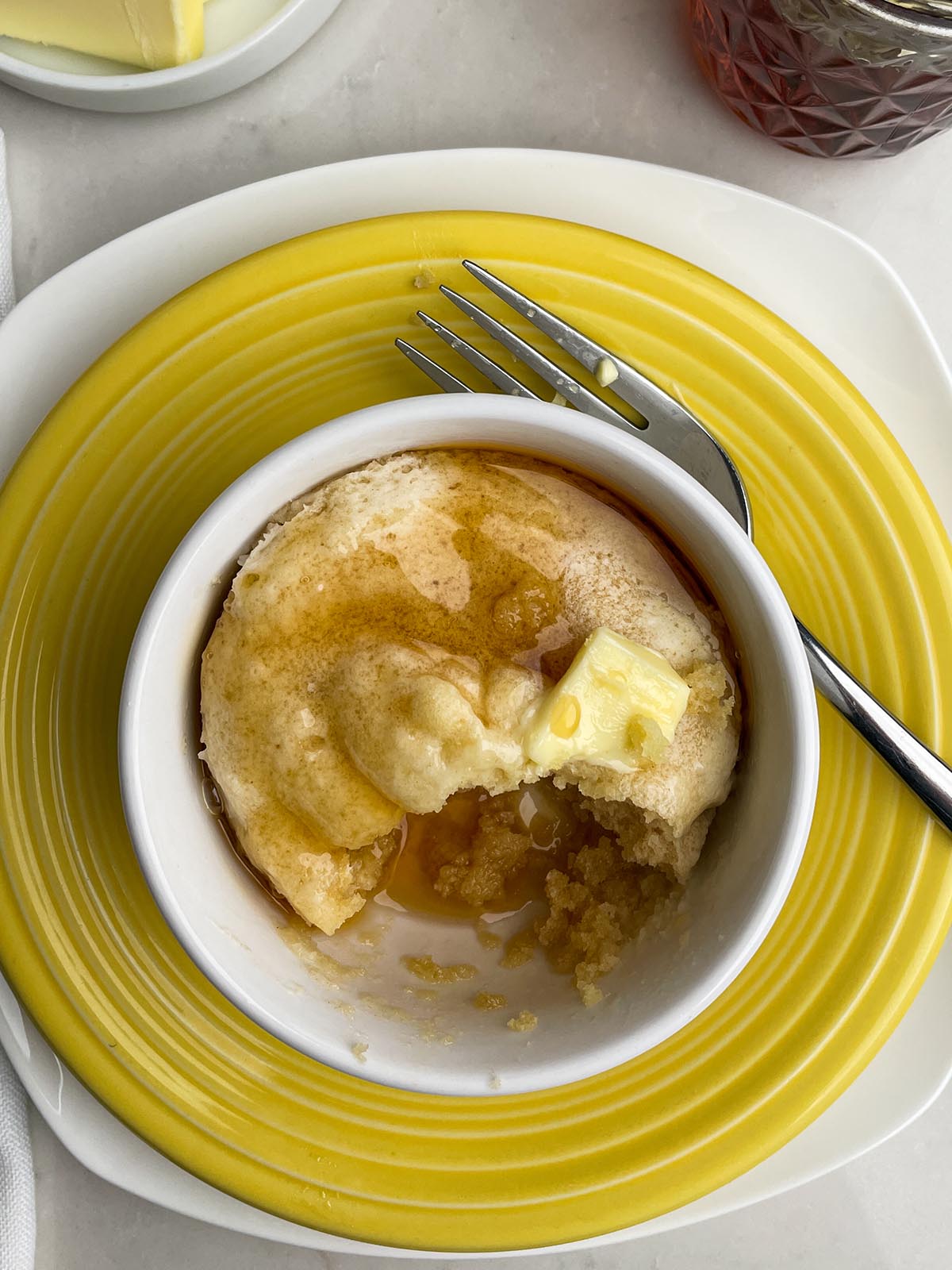Bisquick pancake in a white mug with butter and syrup on a yellow plate