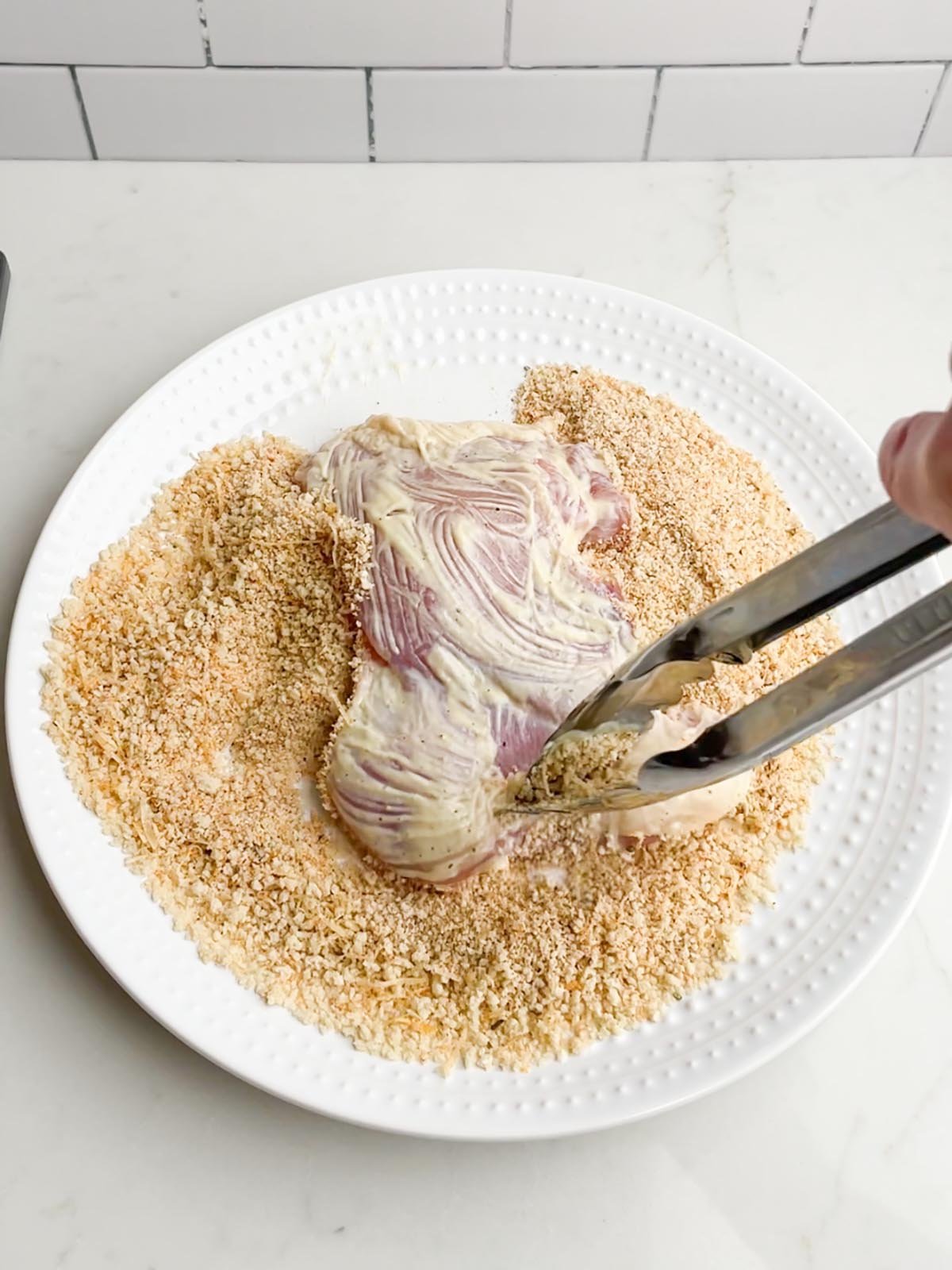 tongs dredging chicken in panko breadcrumb mixture