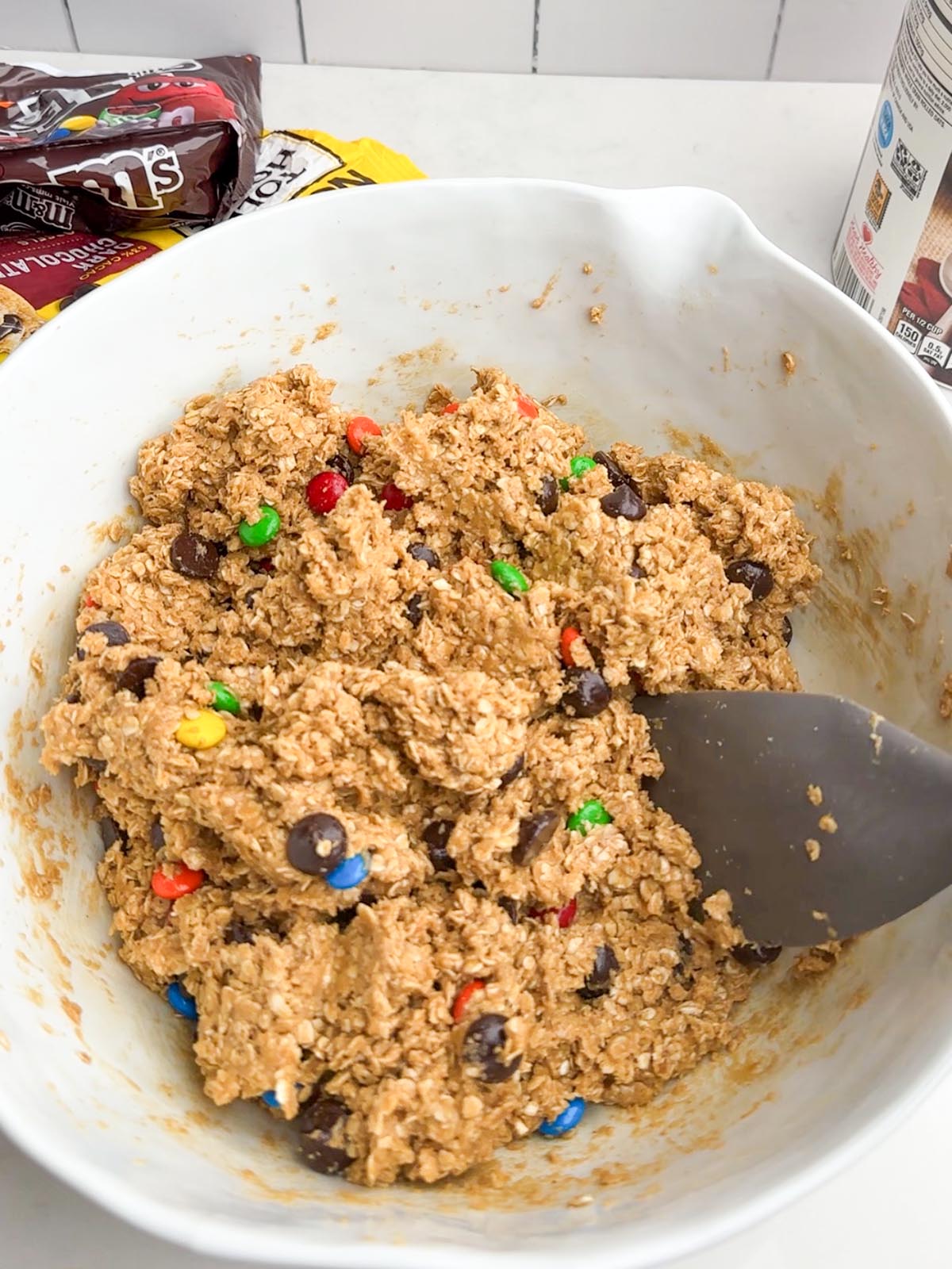 Monster cookie dough with oats, M&Ms, and chocolate chips in a white mixing bowl.