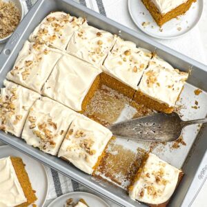 partial pan of pumpkin bars with cream cheese frosting with a cake server resting in the pan