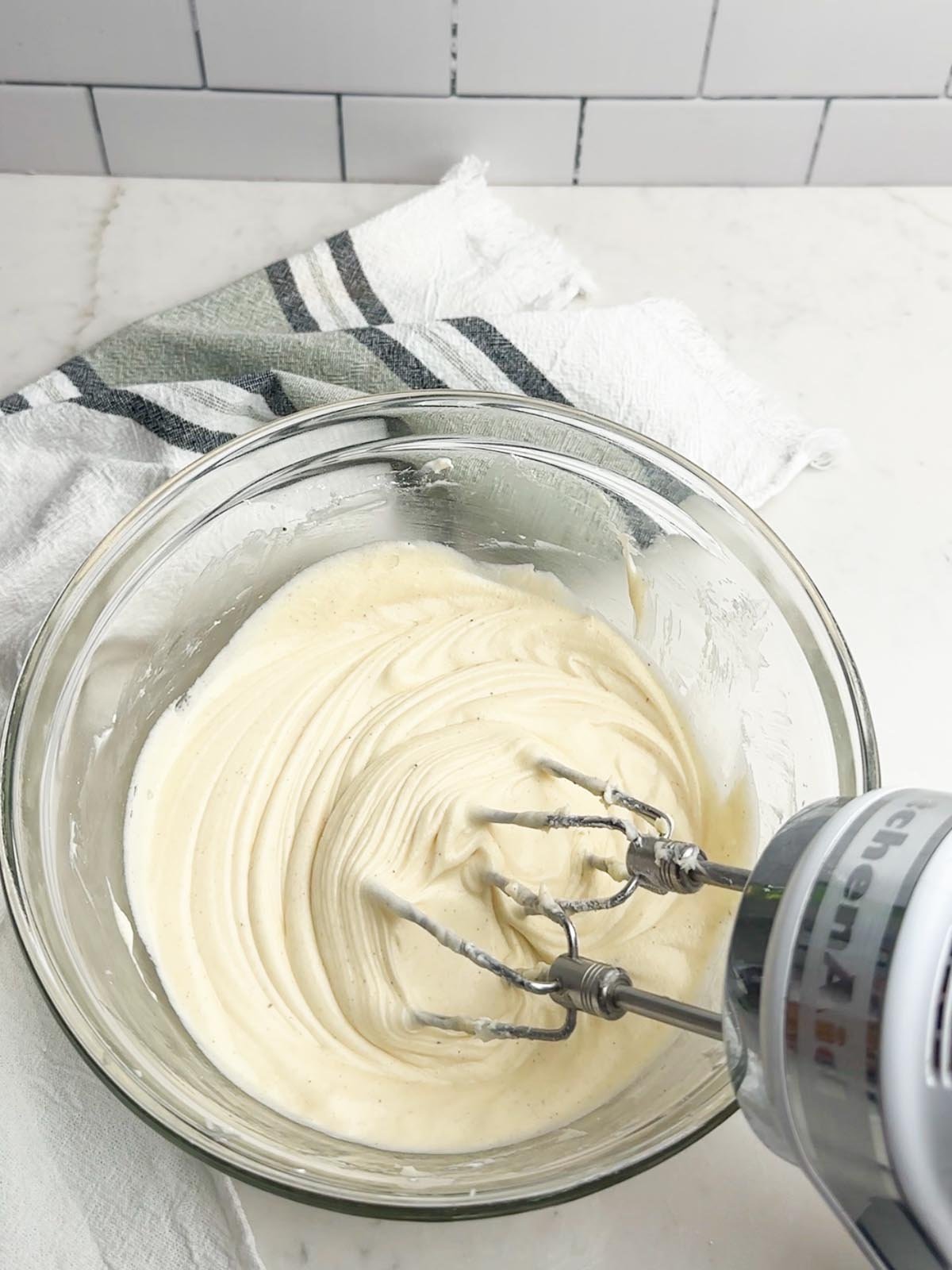 hand mixer mixing cream cheese frosting in a clear bowl